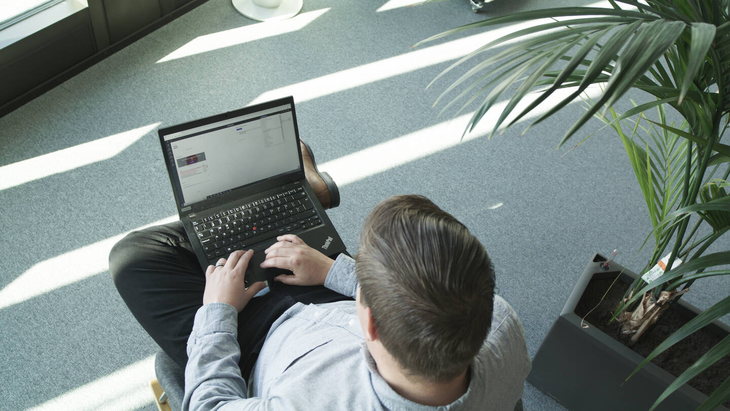 Mann med pc sitter i en stol med en plante på høyre side