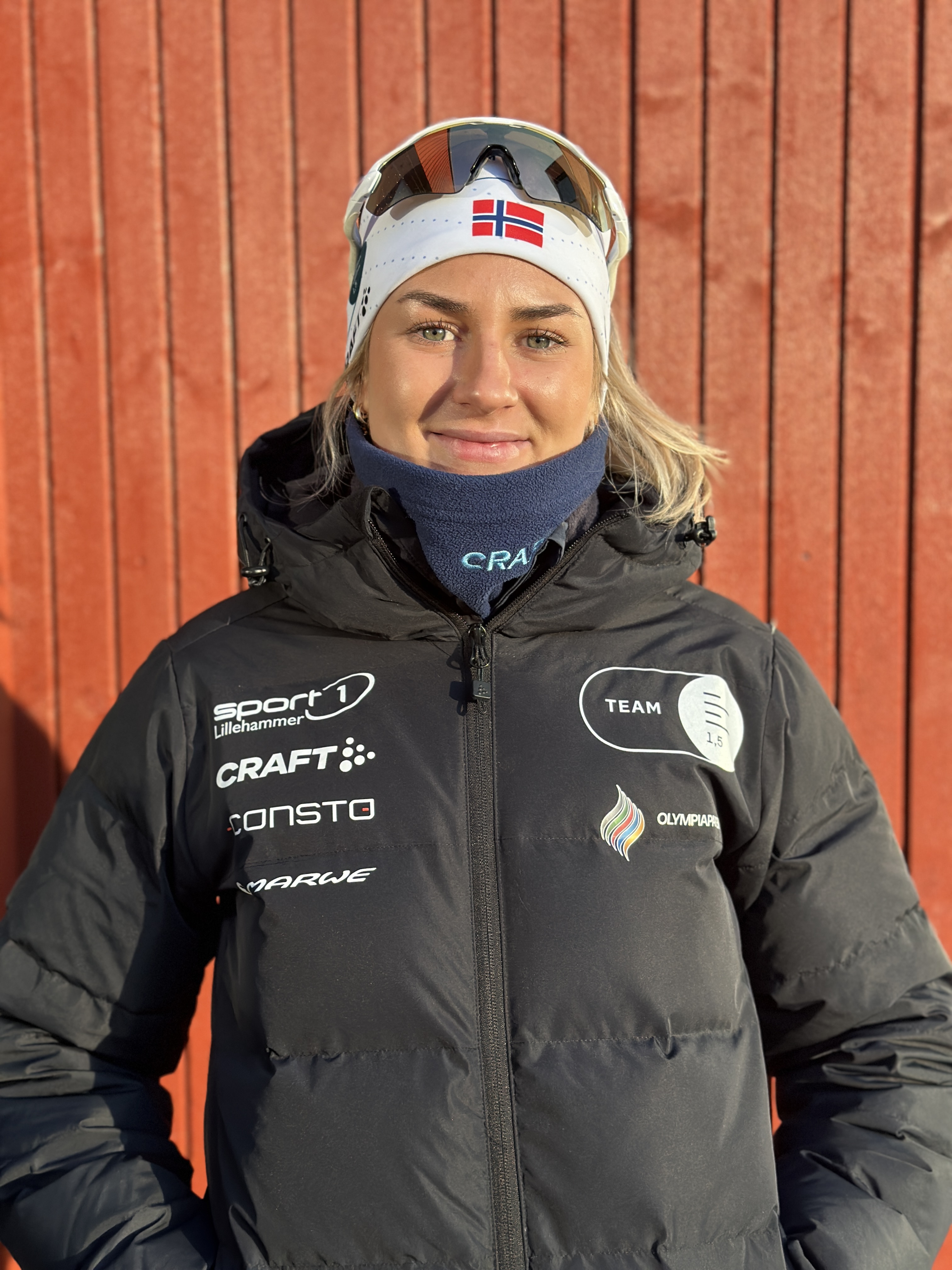 Maren Bakken, Skiskytter, står mot en rød vegg i vintersolen