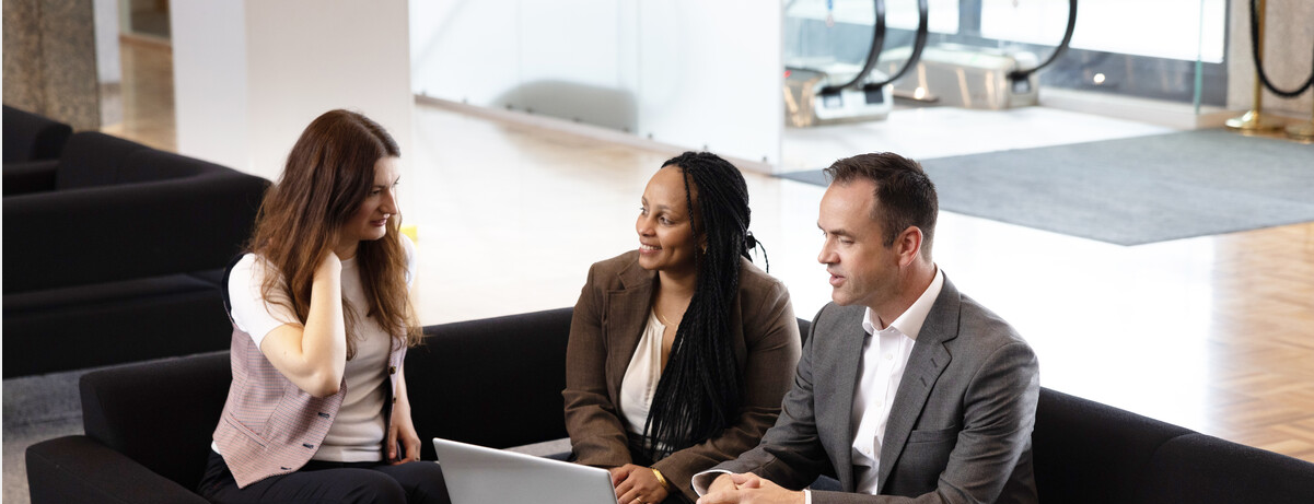 tre kollegaer i fellesarealet som prater over en pc