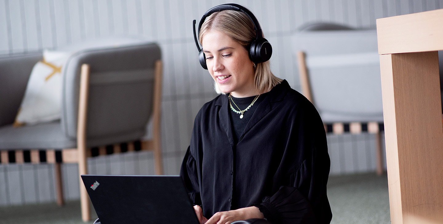 Kvinne som sitter med bena i kryss med pc og headset