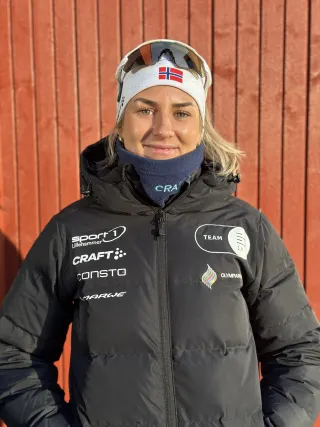 Maren Bakken, Skiskytter, står mot en rød vegg i vintersolen