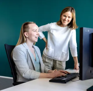 To kvinnlige kolleger som ler mens de ser på en pc skjerm grønn vegg