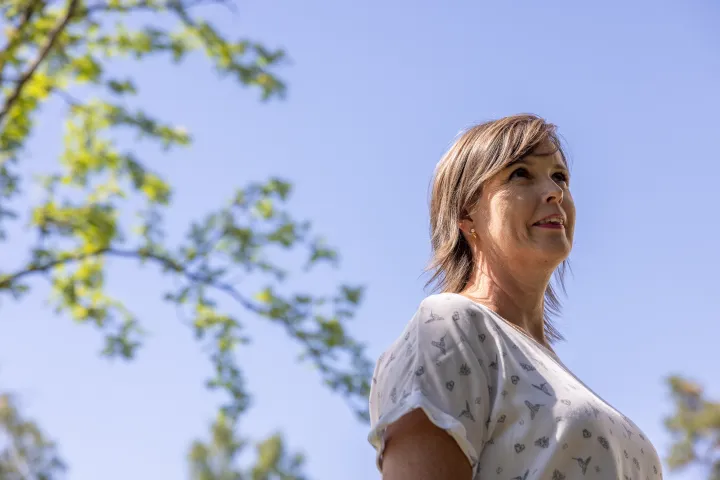 Kvinner som smiler med en blå himmel i bakgrunnen og grønne trær 