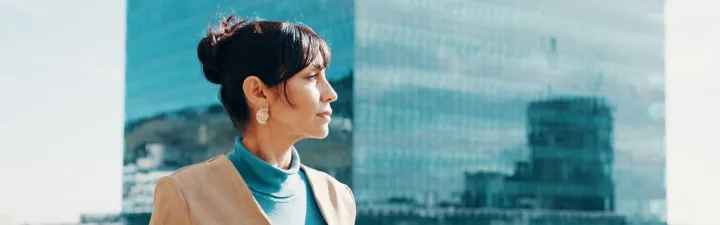 Kvinne som står ute med en skyskraper i bakgrunnen. Hun stirrer utover landskapet. Det er fint vær, muligens litt bris. Hun tenker over neste steg. 