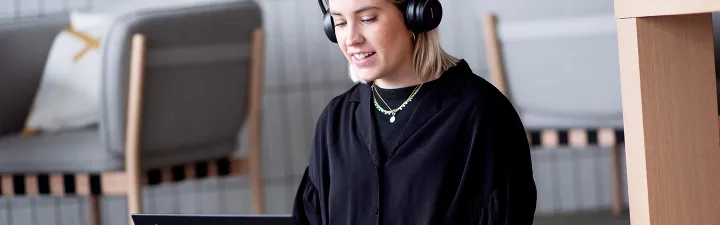 Kvinne som sitter med bena i kryss med pc og headset 