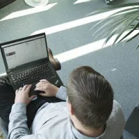 Mann med pc sitter i en stol med en plante på høyre side