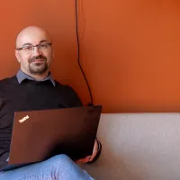 Timo i en sofa med pc. hvit sofa mot rødoransje vegg