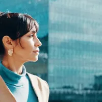 Kvinne som står ute med en skyskraper i bakgrunnen. Hun stirrer utover landskapet. Det er fint vær, muligens litt bris. Hun tenker over neste steg.