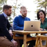 tre kollegaer som sitter sammen foran en mac og diskuterer innholdet i fint sommervær.